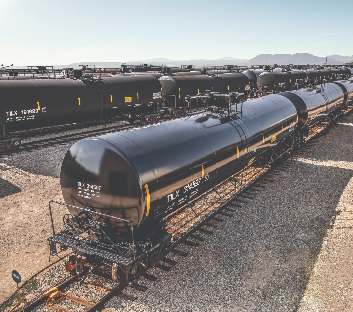 Black tank cars are lined up at a railyard