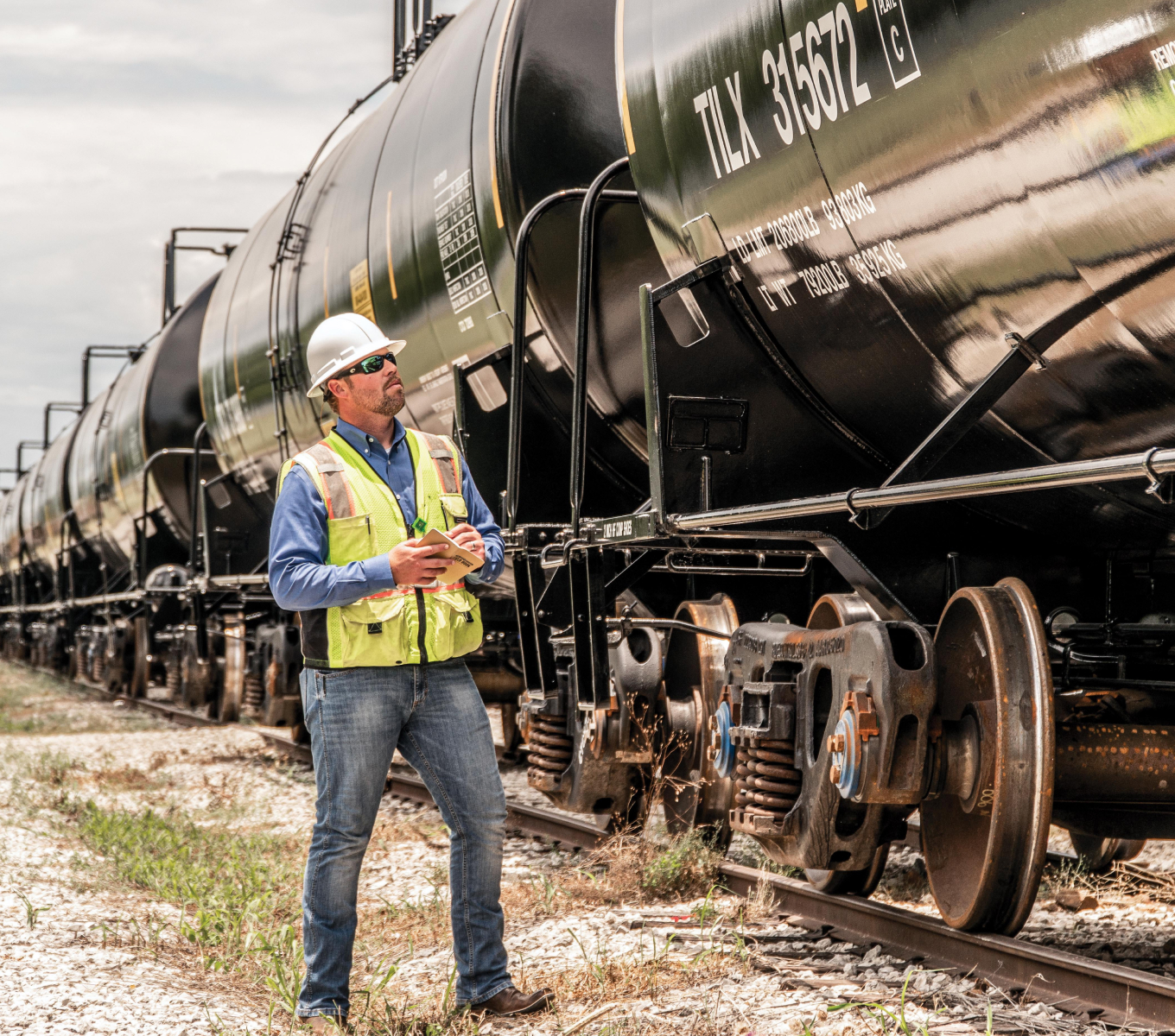 Yellow-vested rail worker inspects a black tank car